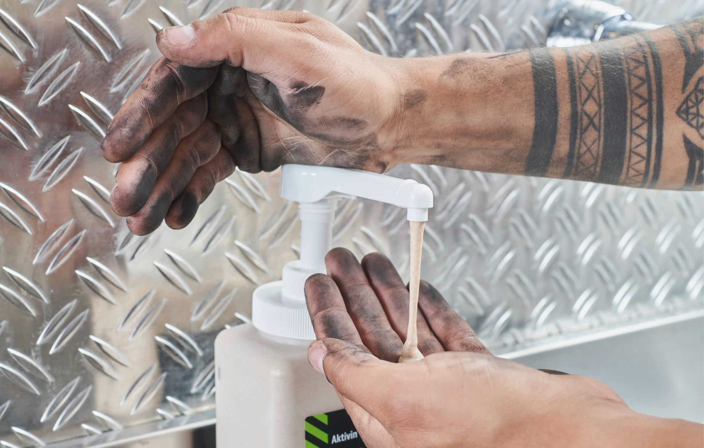 Pumpstöße auf die WERO Handwaschpaste mit verschmutzten Händen. Tätowierter Arm. 