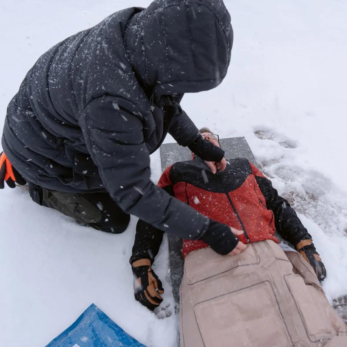 Eine Person leistet Erste Hilfe und deckt eine verletzte Person mit einer Ready-Heat™ - 6-Element-Decke im Schnee, um Unterkühlung vorzubeugen.