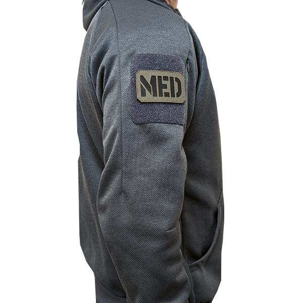 Patch Lasercut MED aus schwarzem Nylon mit MED-Beschriftung, per Reißverschluss an dunklem Hoodie-Ärmel befestigt