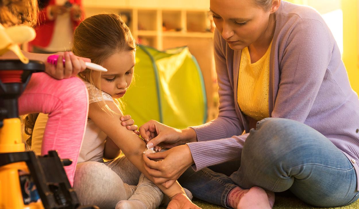 Eine Frau verabreicht einem Mädchen im Klassenraum eine Impfung, während das Kind auf dem Boden sitzt und betreut wird.