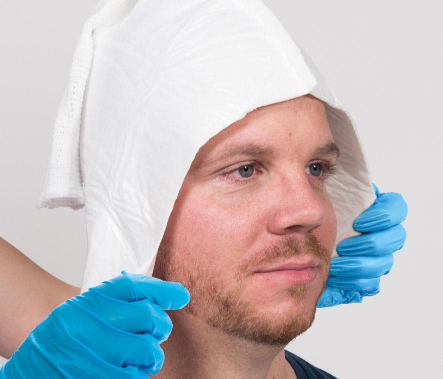 Ein Mann mit weißem Tuch über dem Kopf, hellem Bart und blauen Handschuhen blickt frontal, trägt ein dunkles Oberteil.