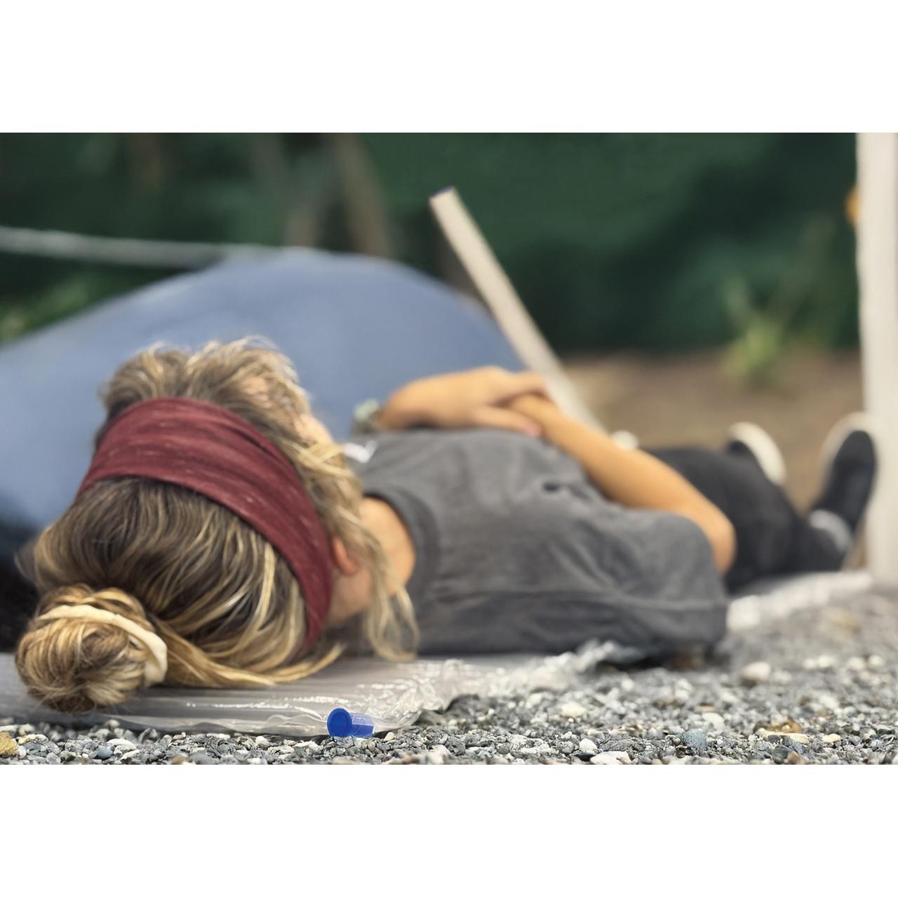 Eine Person liegt ausgestreckt auf der Rescue Essentials® AirBase Aufblasbare Isoliermatte, deren kompakte Form und versiegelte Luftkammern erkennbar sind.