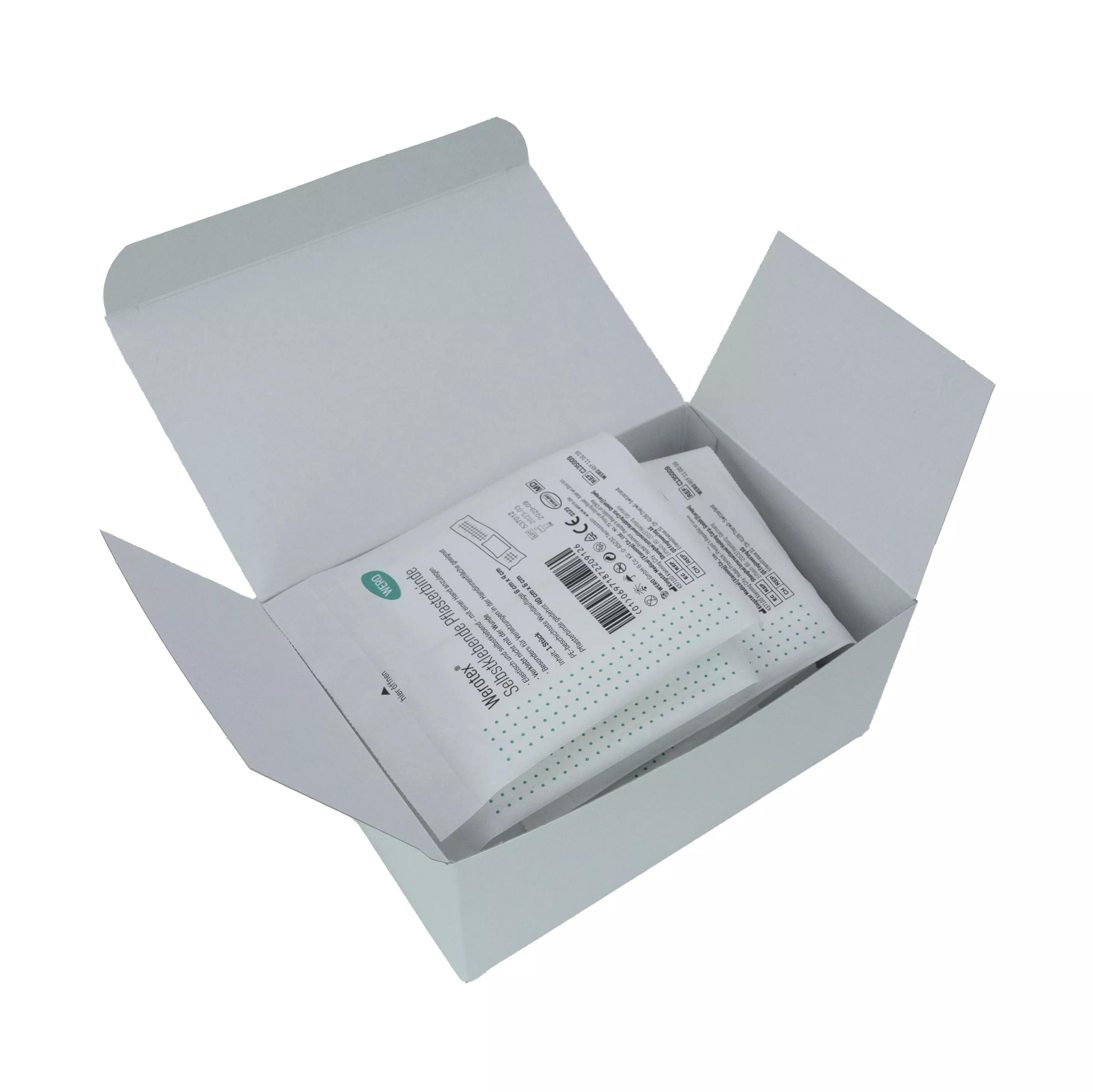 Offene Schachtel mit zwei einzeln verpackten Werotex® selbstklebende Pflasterbinde, steril, mit saugfähiger Wundauflage und elastischer Fixierbinde.