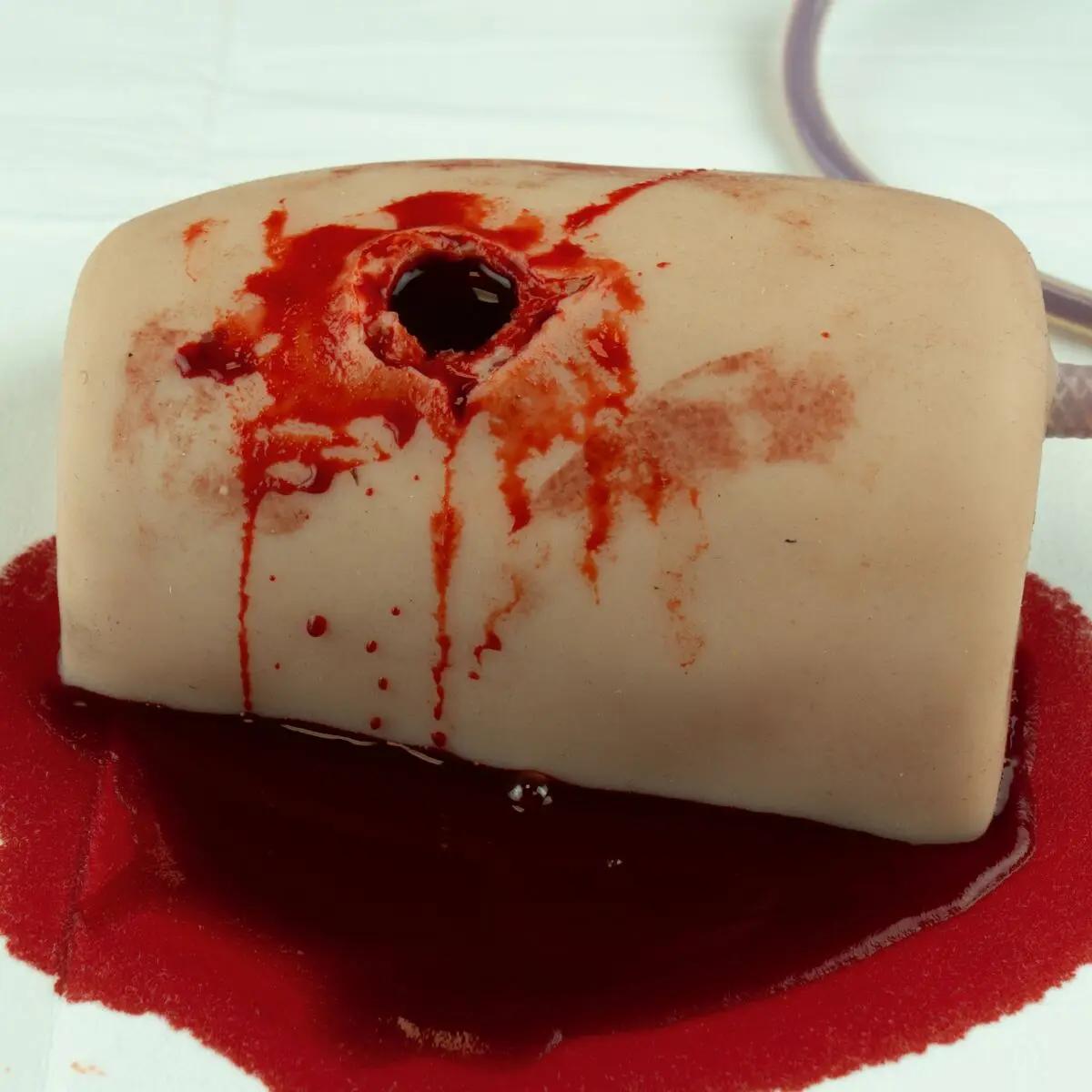 TrueClot® Wound Packing Task Trainer Schusswunden zeigt eine weiße Puppe mit blutähnlichen Flecken und simuliertem Schussloch im Brustbereich.