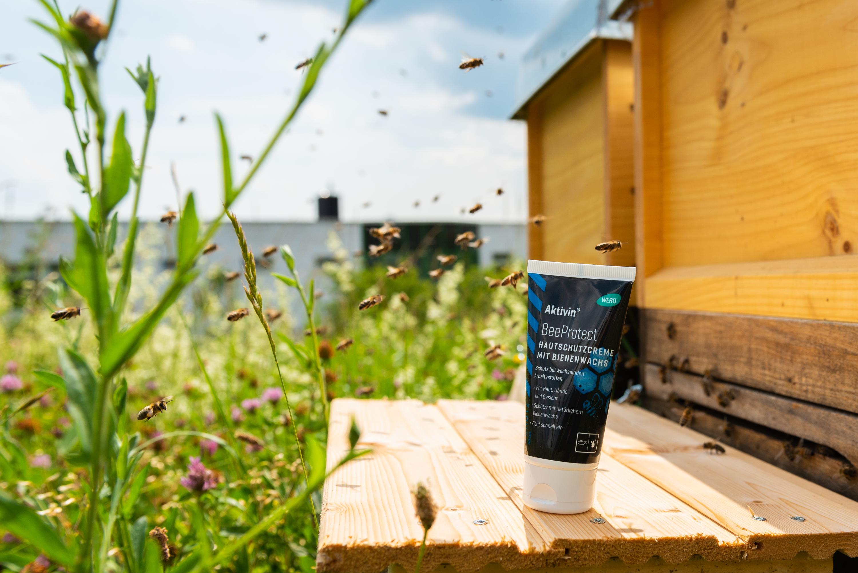 BeeProtect Handcreme-Tube auf Holzbank, umgeben von fliegenden Bienen, Blumen und grünem Gartenhintergrund