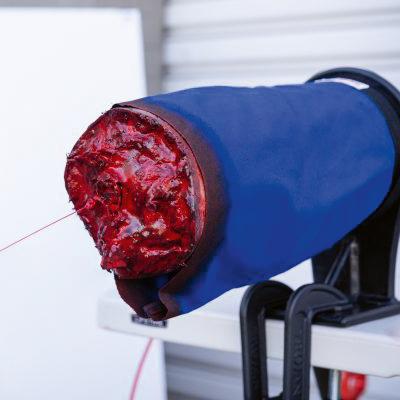 Blauer TRAUMASIM® Emergency Tourniquet Trainer mit braunem Rand, rotem Kabel und schwarzer Klemme zur Simulation von Blutungskontrolle.