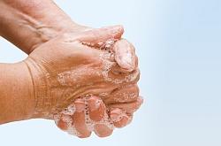 Zwei Hände mit hellbrauner Haut werden unter fließendem Wasser gründlich mit Seife eingewaschen, Schaum bedeckt die Haut.