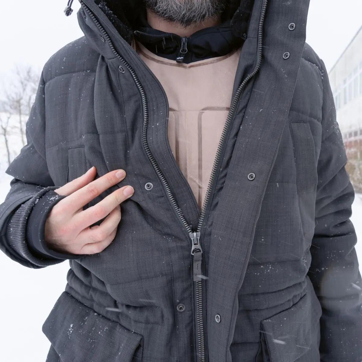 Ein Mann trägt eine beige Ready-Heat™ - Weste mit durchgehendem Reißverschluss über einem hellen Shirt in einer verschneiten Umgebung.