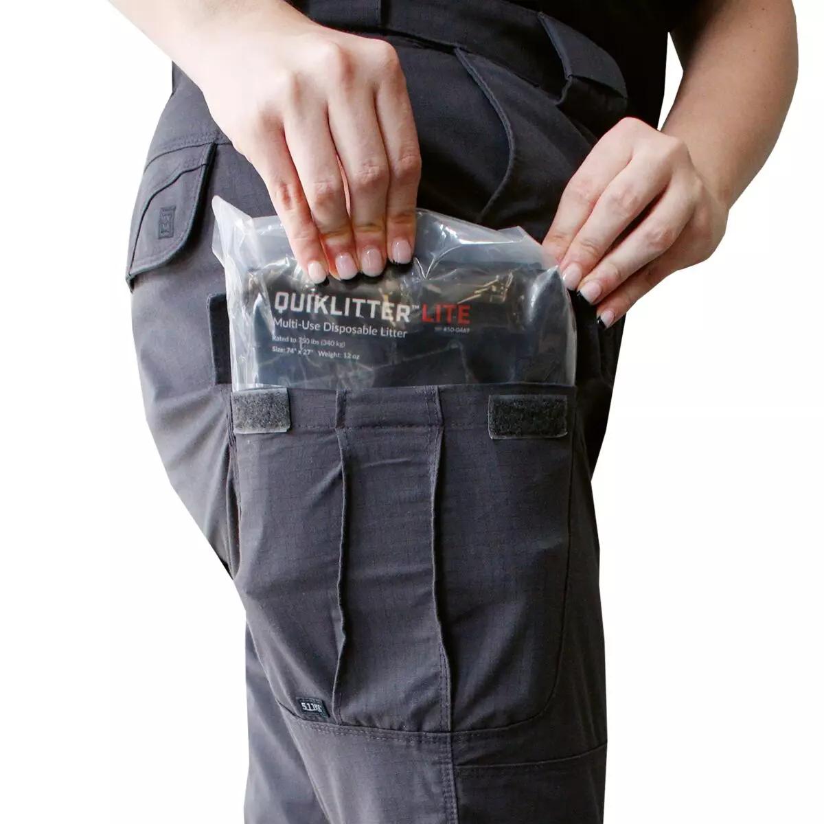 Eine Person verstaut einen Rescue Essentials QuikLitter™ Lite Tragetuch-Beutel mit 10 Tragegriffen, leichtem Gewicht und robuster Verarbeitung in einer schwarzen taktischen Hose.