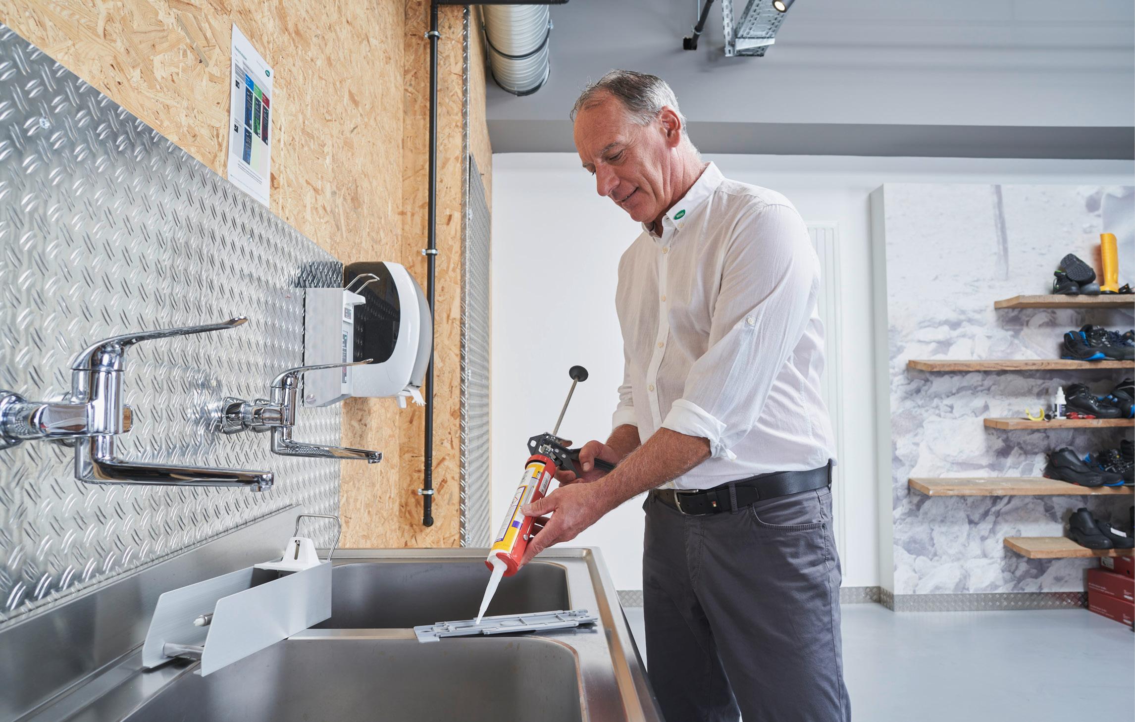 Ein WERO Mitarbeitender trägt mit einer Spritze Silikon auf die Halterung eines Spenders auf 