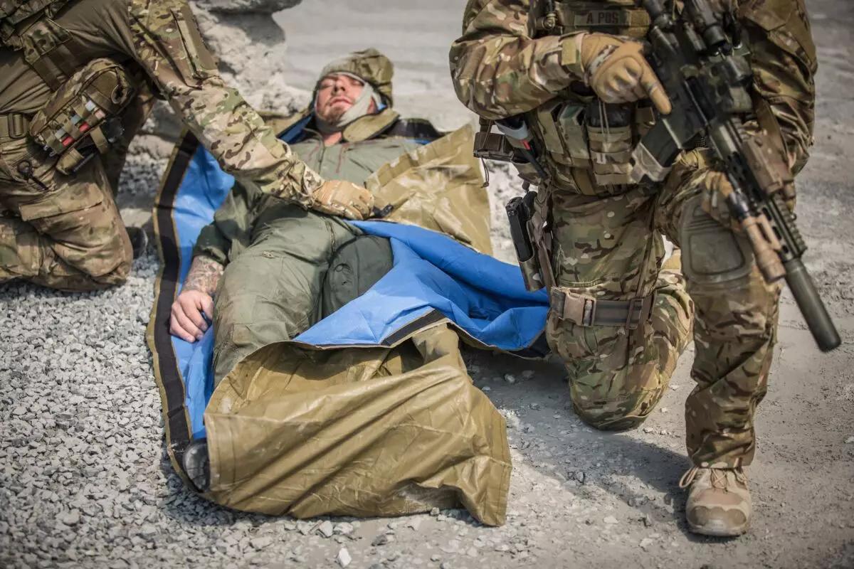 Ein Soldat legt im Gelände eine blaue, reflektierende NAR Hypothermia Prevention and Management Kit (HPMK®) Decke über einen verletzten Kameraden.
