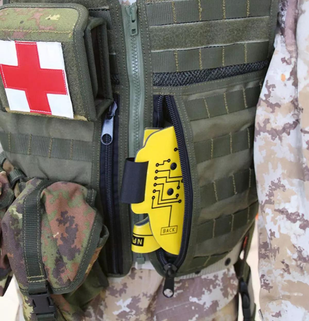 Ein Soldat mit Sanitätsabzeichen zeigt am geöffneten Notfallfach seines Westen einen gelben Immobilisationskragen Necklite™, flexibel faltbar mit Aluminium-Schaumstoff.