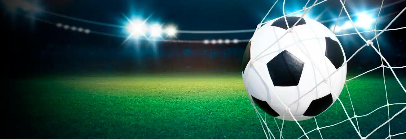 Ein weiß-schwarzer Fußball liegt auf grünem Rasen vor einem gespannten Tornetz, beleuchtet von Stadionlichtern.