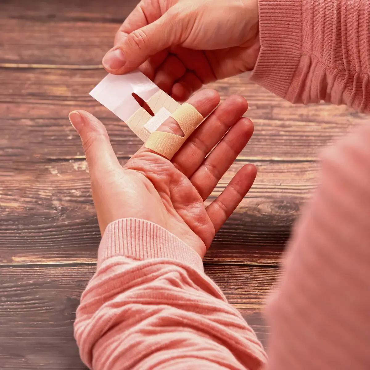 Eine Hand in rosafarbenem Pullover hält ein Fingergelenkpflaster Weroplast® MasterTex aus anpassungsfähigem, textilem Gewebe mit runder Aussparung.