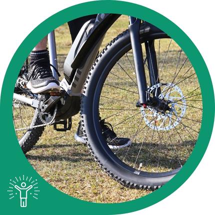 Schwarzes E-Bike mit Speichenrädern, Scheibenbremse und einer darauf sitzenden Person.