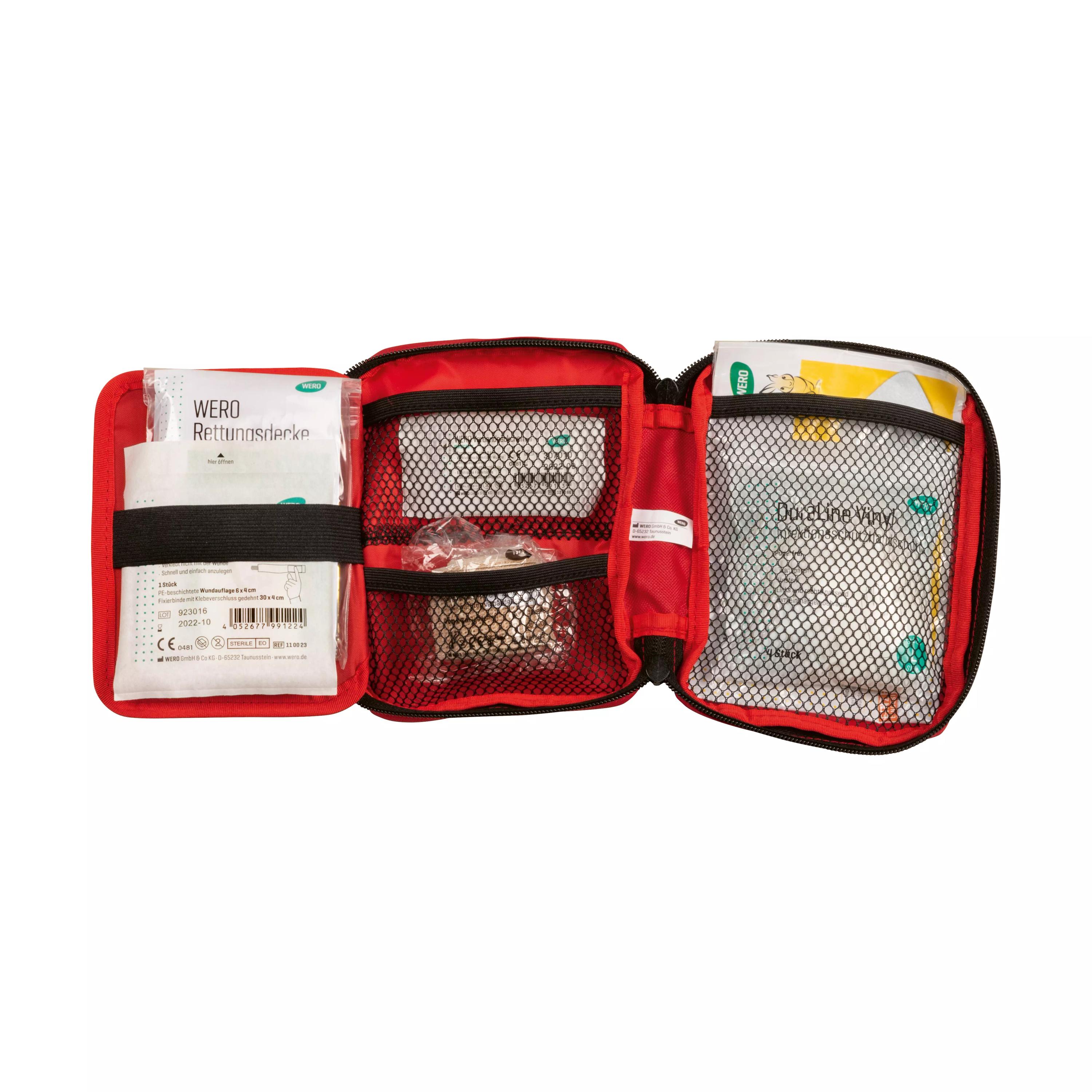 Ein aufgeschlagenes Erste-Hilfe-Set in Rot-Schwarz zeigt zwei Fächer mit etikettierten Verbandsmaterialien und Sicherheitsinformationen auf Weißem Hintergrund.