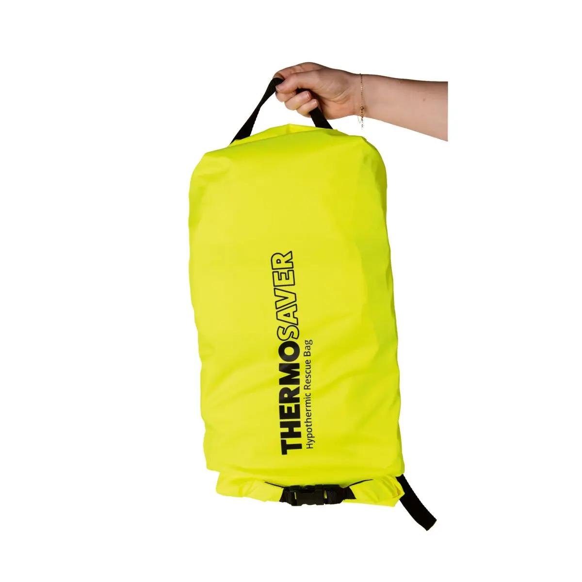 Eine Hand hält den Tragegriff der Thermosaver Hypothermic Rescue Bag - Neongelb mit schwarzem Text, schwarzen Gurten und Clip, wasserabweisender Außenschicht und isolierender Polsterung.