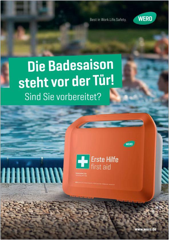 Oranger Erste-Hilfe-Kasten mit Aufschrift „Erste Hilfe first aid“ steht am Rand eines Schwimmbeckens, Wasser und Personen unscharf im Hintergrund.