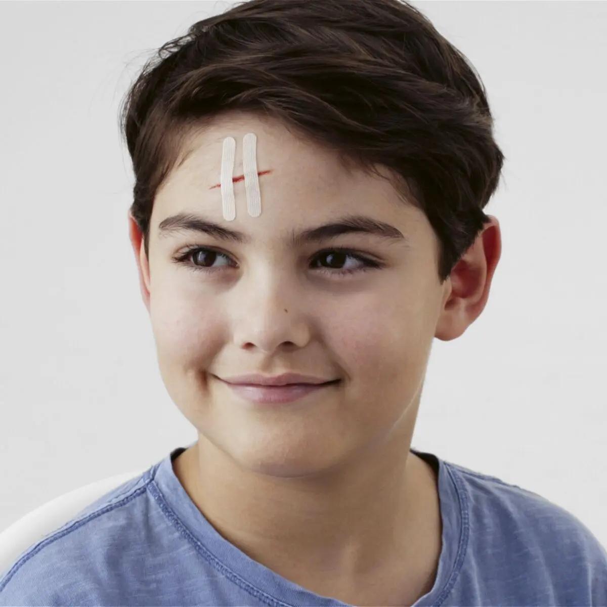 Ein Junge mit frischer Stirnwunde trägt Leukoplast® Wundnahtstreifen - Größe XS, die hautfreundlich, atmungsaktiv und formstabil anliegen.