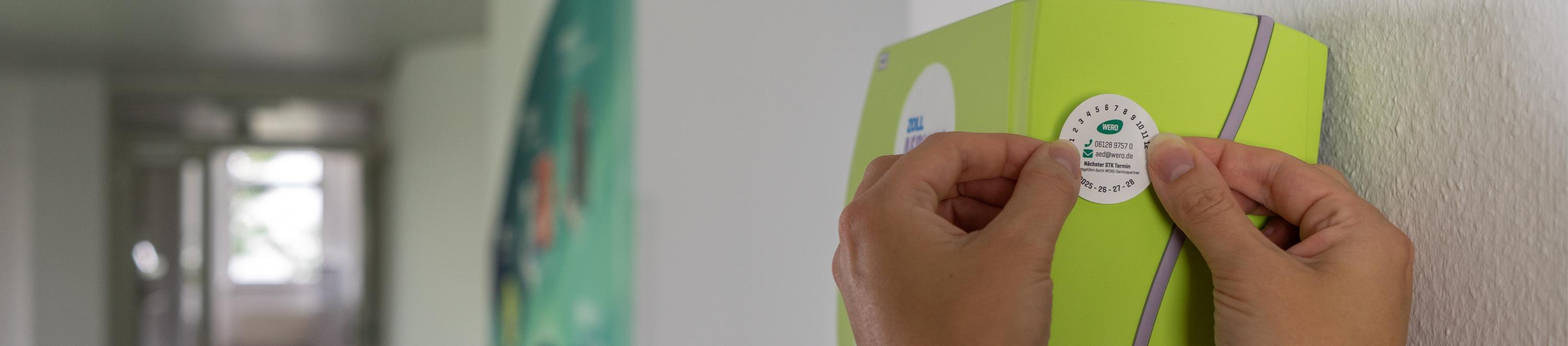 Auf einen AED wird eine STK-Prüfplakette geklebt.