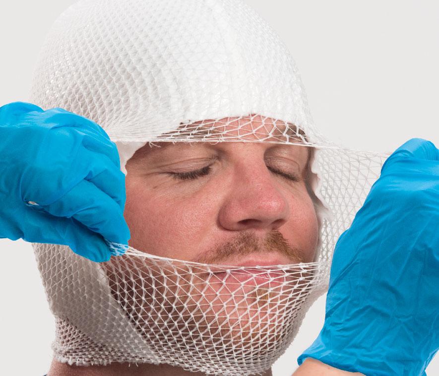 Ein Mann mit geschlossen Augen trägt eine weiße Netzhaube sowie eine weiße Gesichtsbandage und blaue Handschuhe.