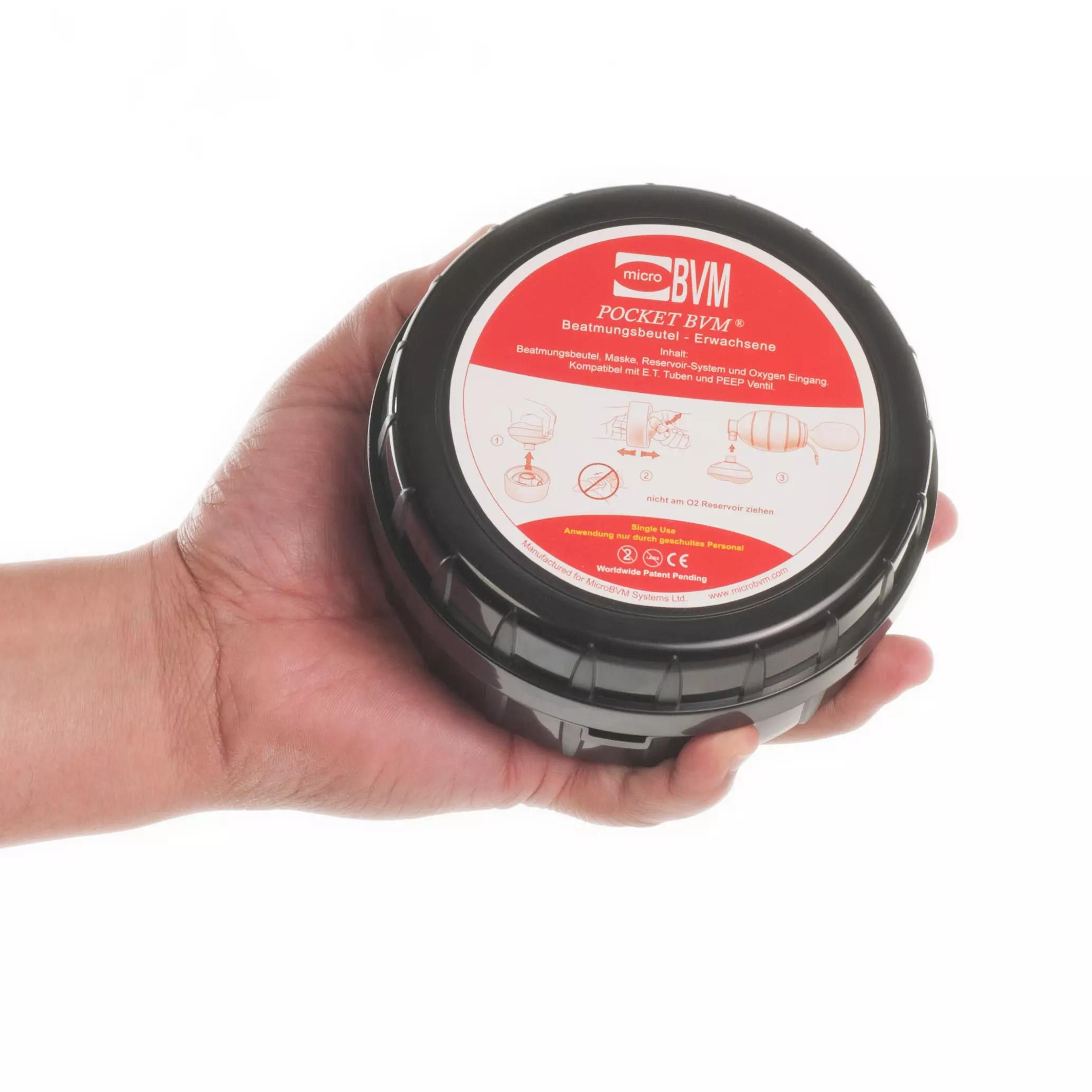 Ein Kompakter Einmal-Beatmungsbeutel Pocket BVM® im schwarzen zylindrischen Behälter mit rotem Etikett wird in einer Hand gehalten.