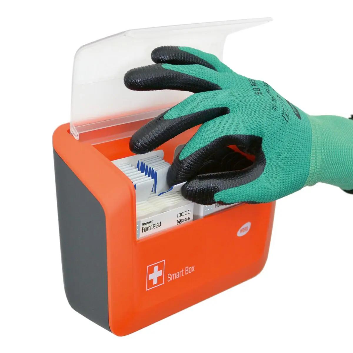 Eine grün behandschuhte Hand öffnet die WERO Smart Box® Pflasterspender gefüllt mit elektromagnetisch detektierbaren, blauen Pflasterstrips.