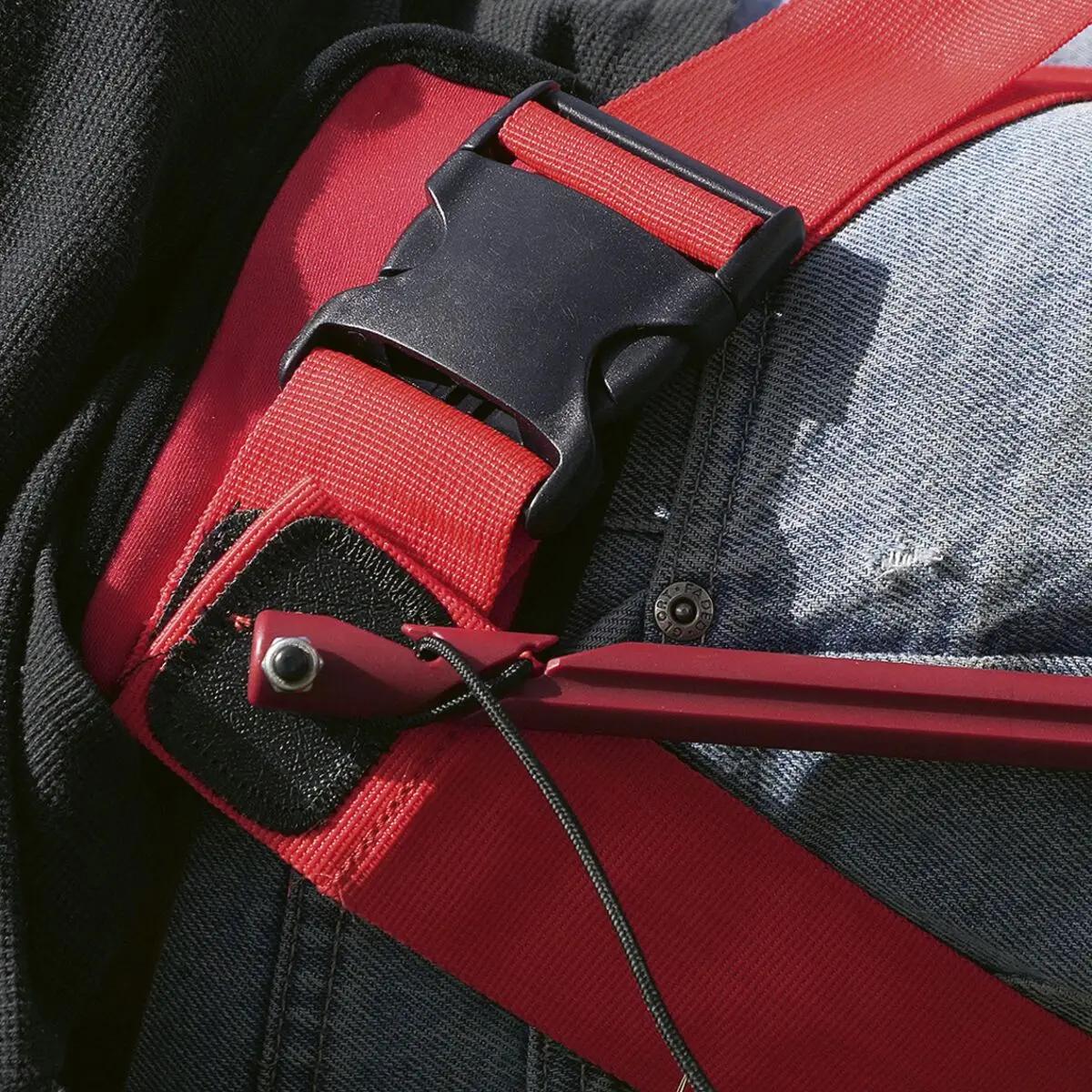 Rotes Slishman Traction Splint (STS) GEN. 2 Sicherheitsgeschirr mit schwarzem Verschluss, sichtbarem Befestigungsseil und rotem Haken an dunkler Jacke angelegt.