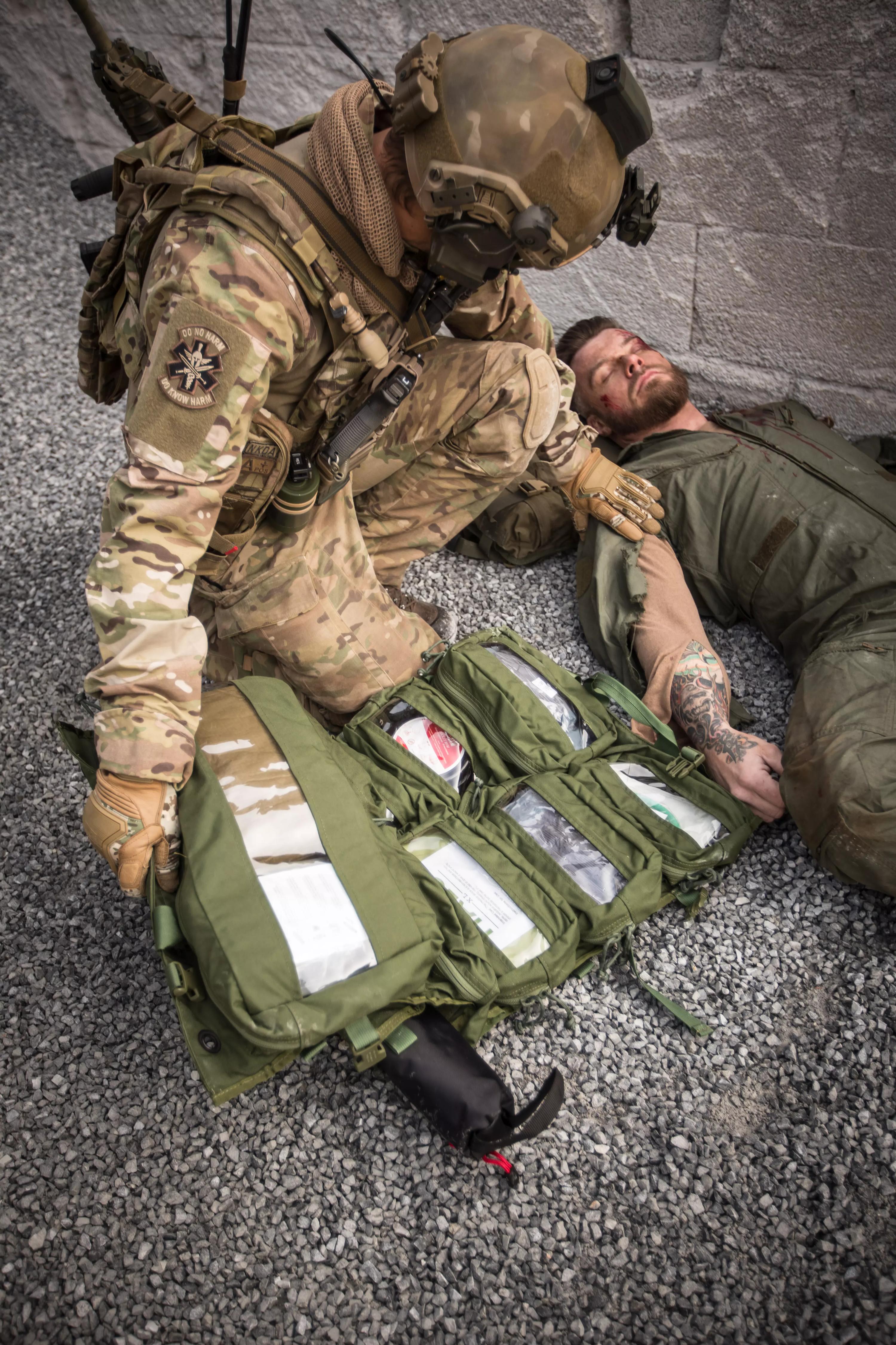 Ein Soldat nutzt eine geöffnete NAR Medic Trauma Sheet Bag – Grün aus 500D CORDURA®, um medizinische Versorgung bei einer verletzten Person zu leisten.