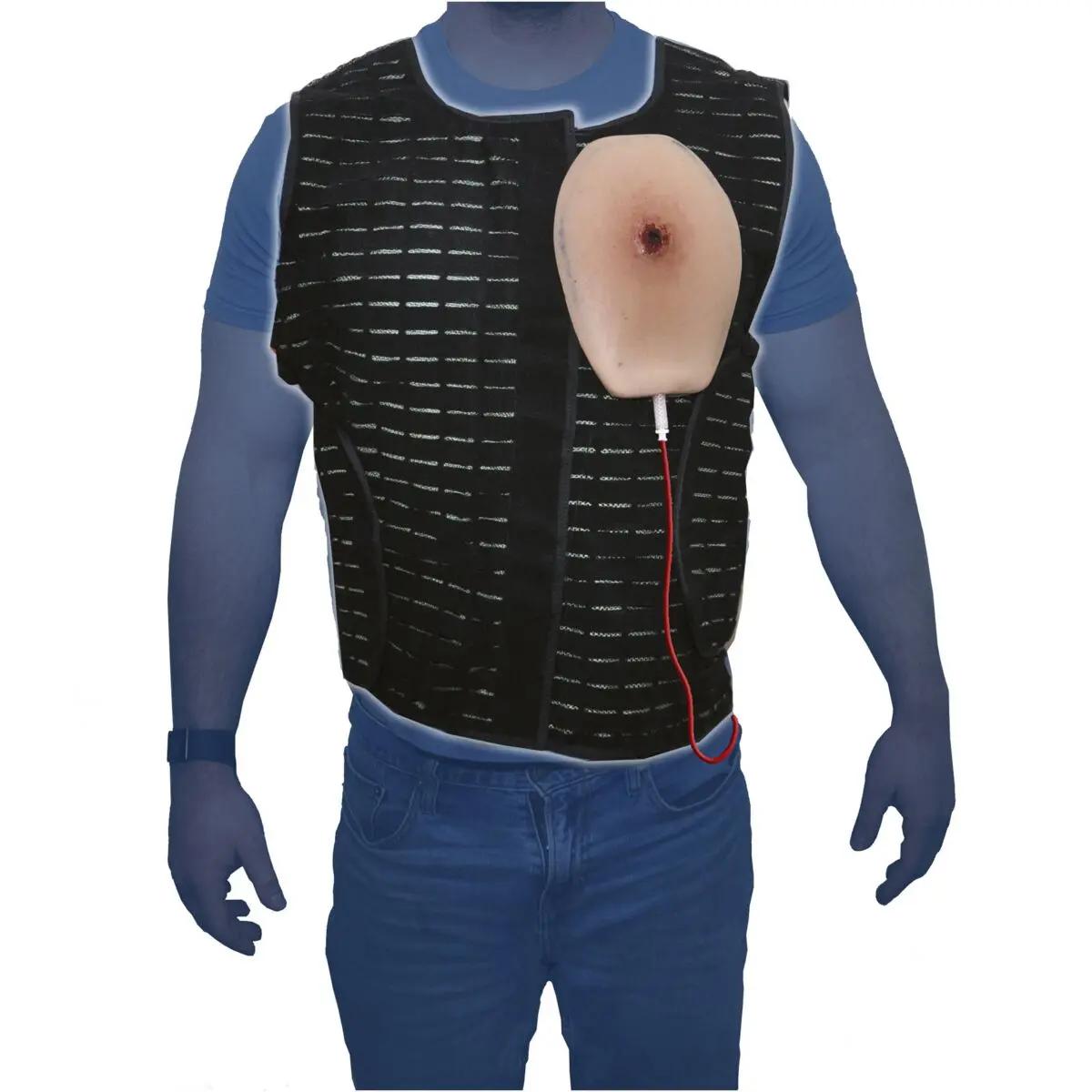 Eine Person trägt einen TrueClot® Chest Seal Application Trainer mit einer realistisch gestalteten Brustwunde und einem roten Kabel auf einer schwarzen Weste.