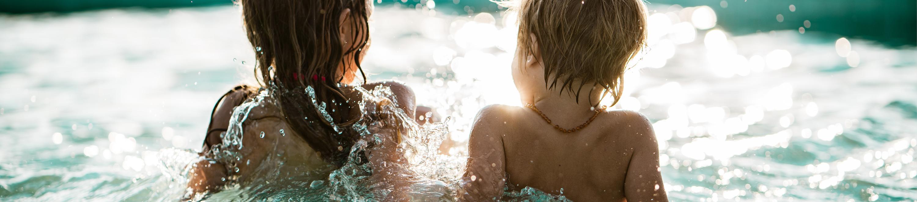 Zwei Kinder sitzen nebeneinander im Wasser.