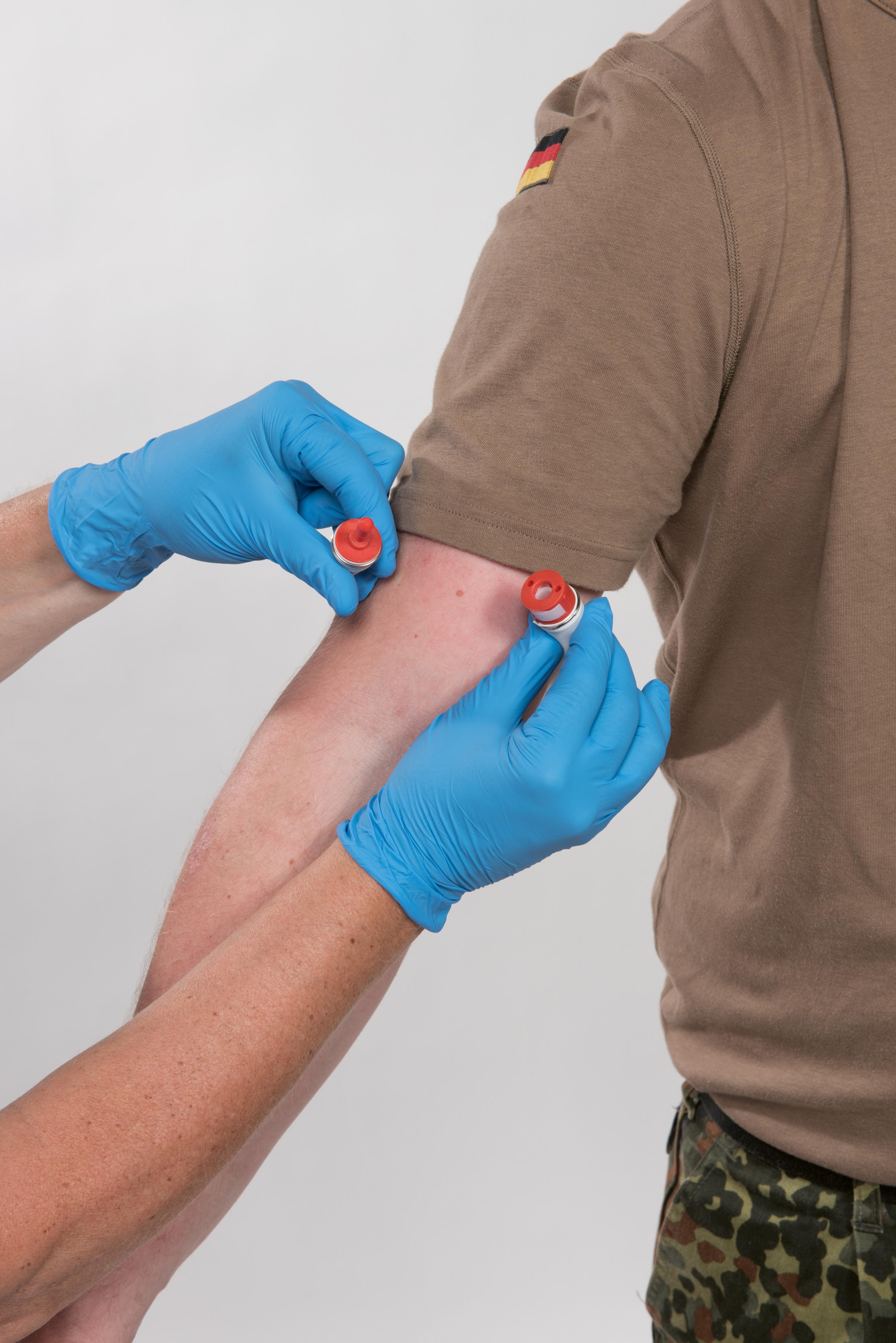 Eine Person trägt den NAR BOA® Standard - 19 cm am Oberarm und erhält mit blauer Spritze und Violetten Vial eine Injektion nahe der Achselhöhle.