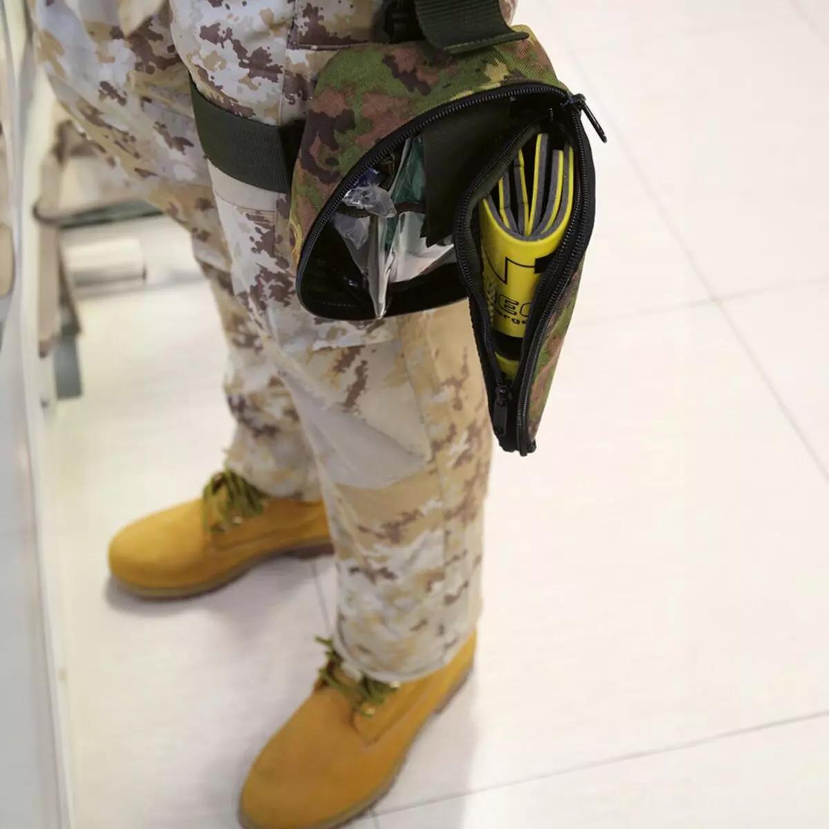 Eine Person in Tarnuniform trägt einen gelben Immobilisationskragen Necklite™ sichtbar in einer schwarzen Tasche, das Modell ist faltbar und bietet sicheren Halt.