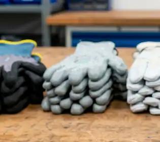 Zwei Stapel grauer, gebrauchter Gummihandschuhe liegen gefaltet auf einer hellbraunen Holzarbeitsfläche.