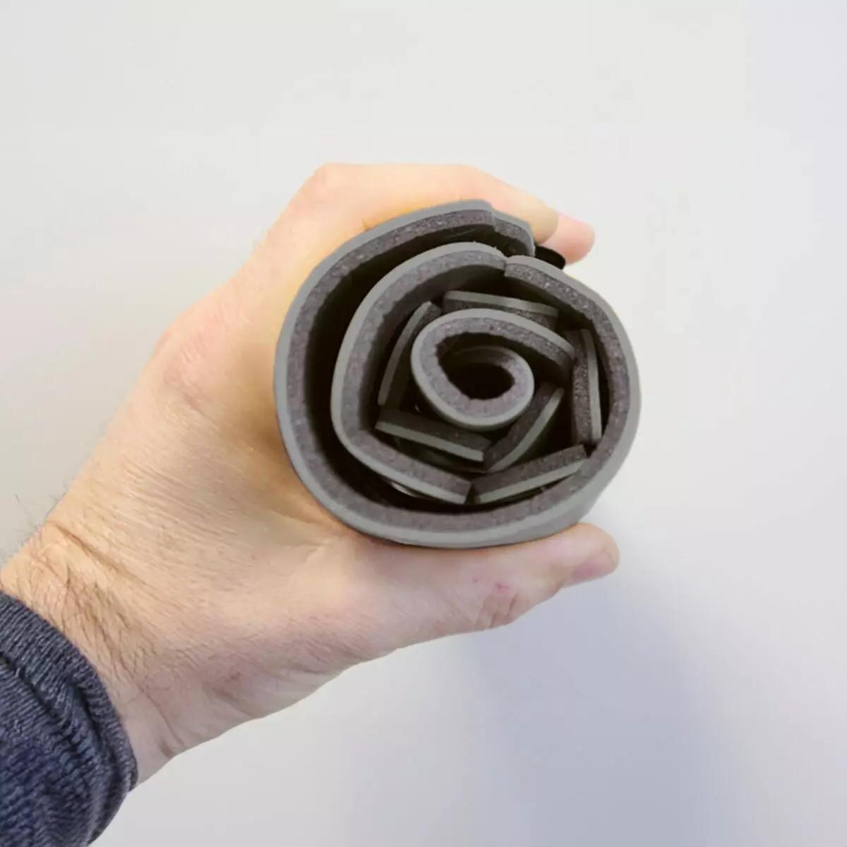 Eine Hand hält einen kompakten, zusammengerollten Immobilisationskragen Necklite™ - Grau mit grauer PU-Schaum-Oberfläche und flexiblem Aluminiumkern.