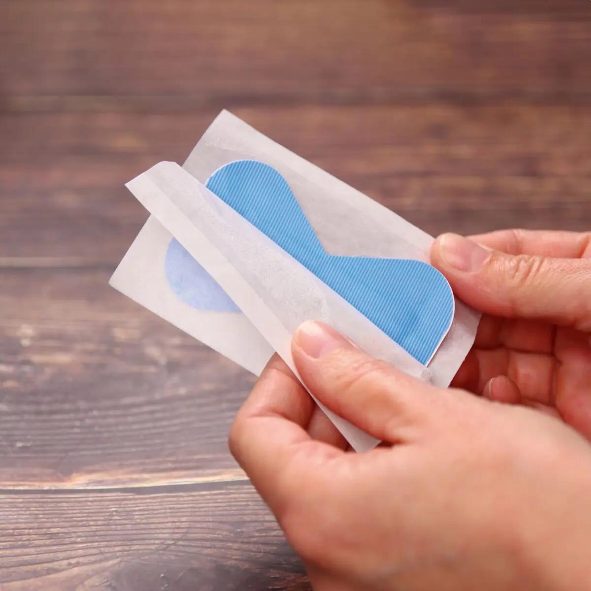 Zwei Hände falten Papier, das ein flexibles, blaues Weroplast® AquaFlex Detect Pflaster mit Aluminiumstreifen und wasserdichter Folie zeigt.