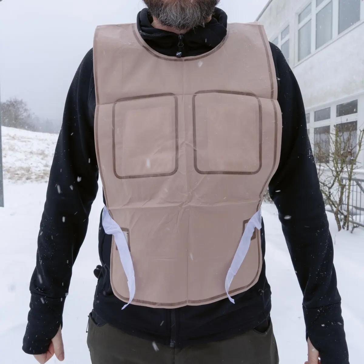 Eine Person trägt im Schnee eine beige Ready-Heat™ - Weste mit zwei braumumrandeten Taschen und sichtbaren weißen Bindebändern.
