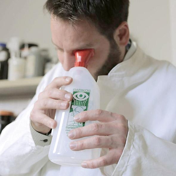Ein Mann in Laborkittel hält eine Augenspülflasche Barikos KS, 620 ml mit rotem Ausguss nahe an sein Auge, bereit zur Anwendung.