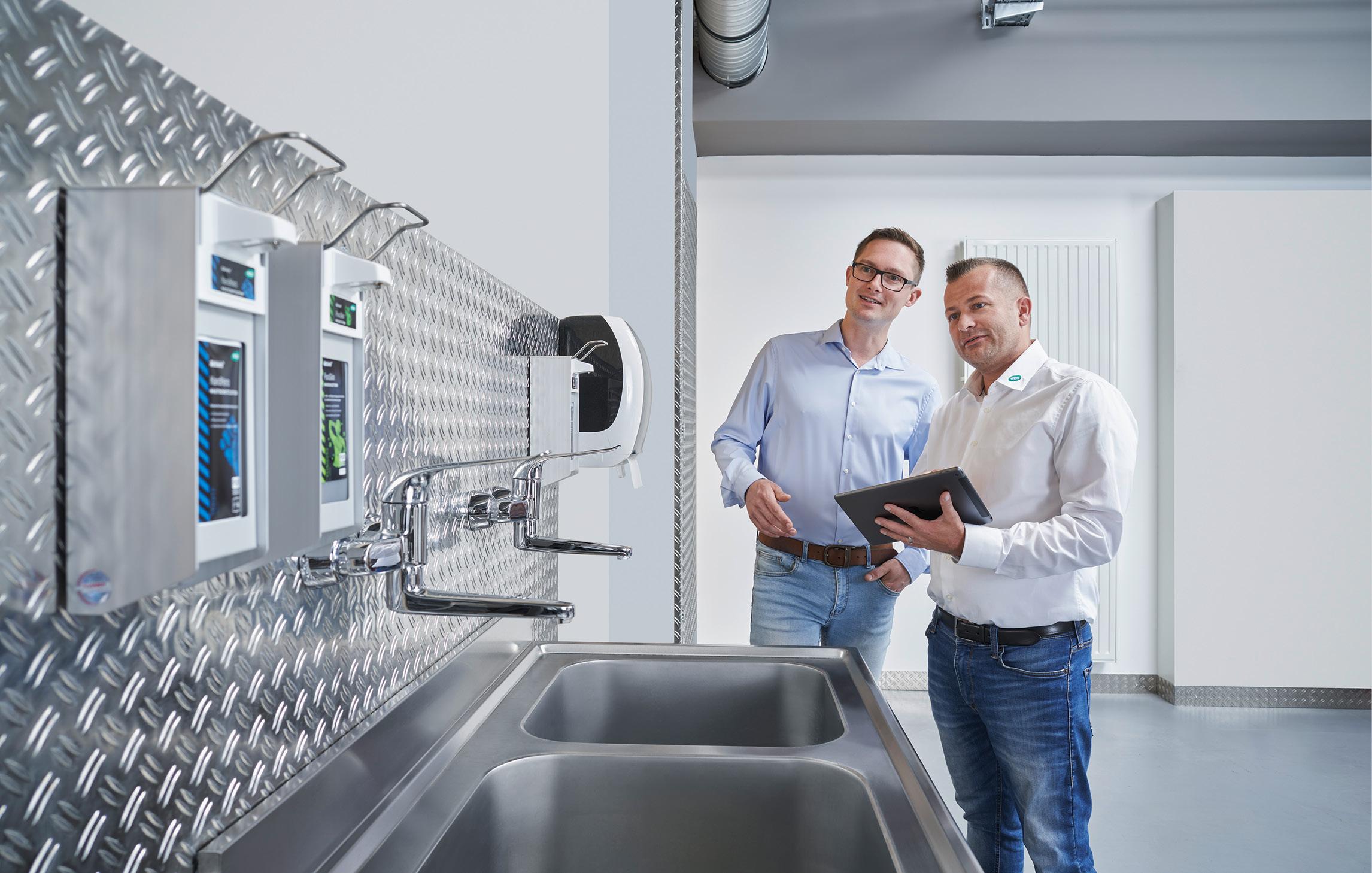 Ein WERO Mitarbeitender begutachtet mit einem Kunden den Waschplatz mit den installierten Spendersystemen