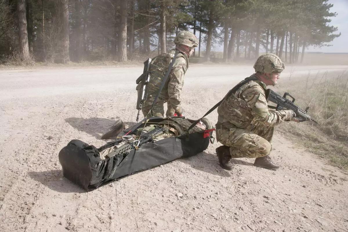 Zwei Soldaten in Tarnuniform und Helm nutzen das Xtract™ SR Module, während sie auf einem Waldweg einen Kameraden auf einer Trage bergen.