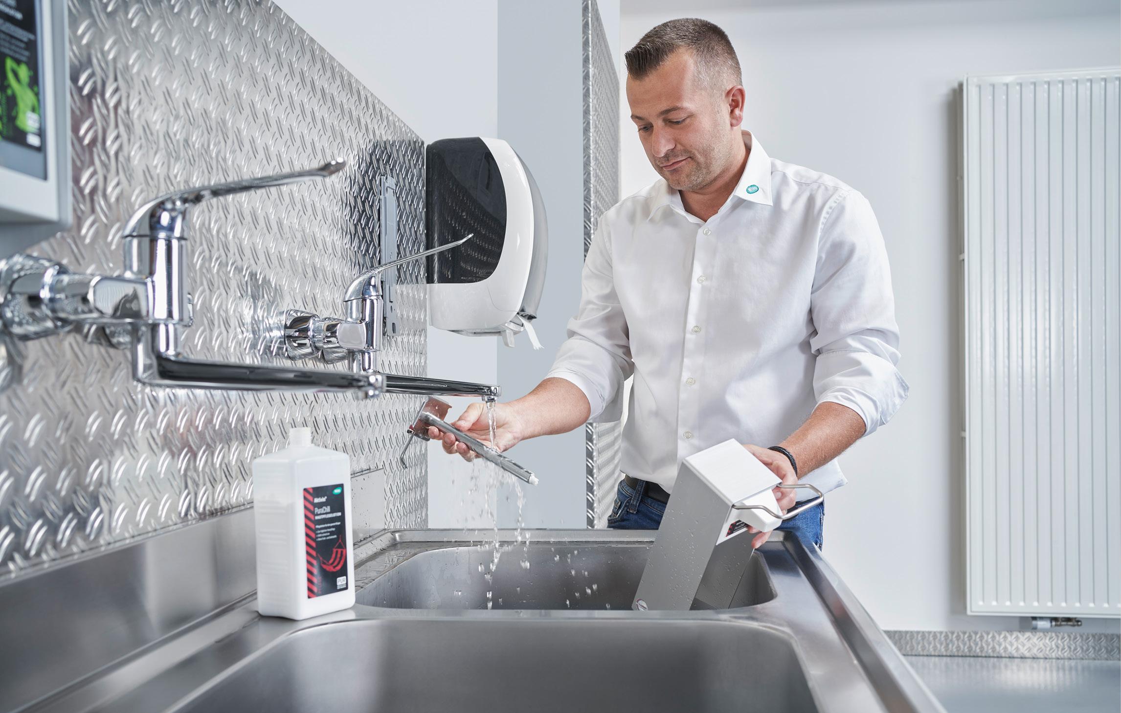 Ein WERO Mitarbeitender reinigt einen Spender in einem metallenen Waschbecken