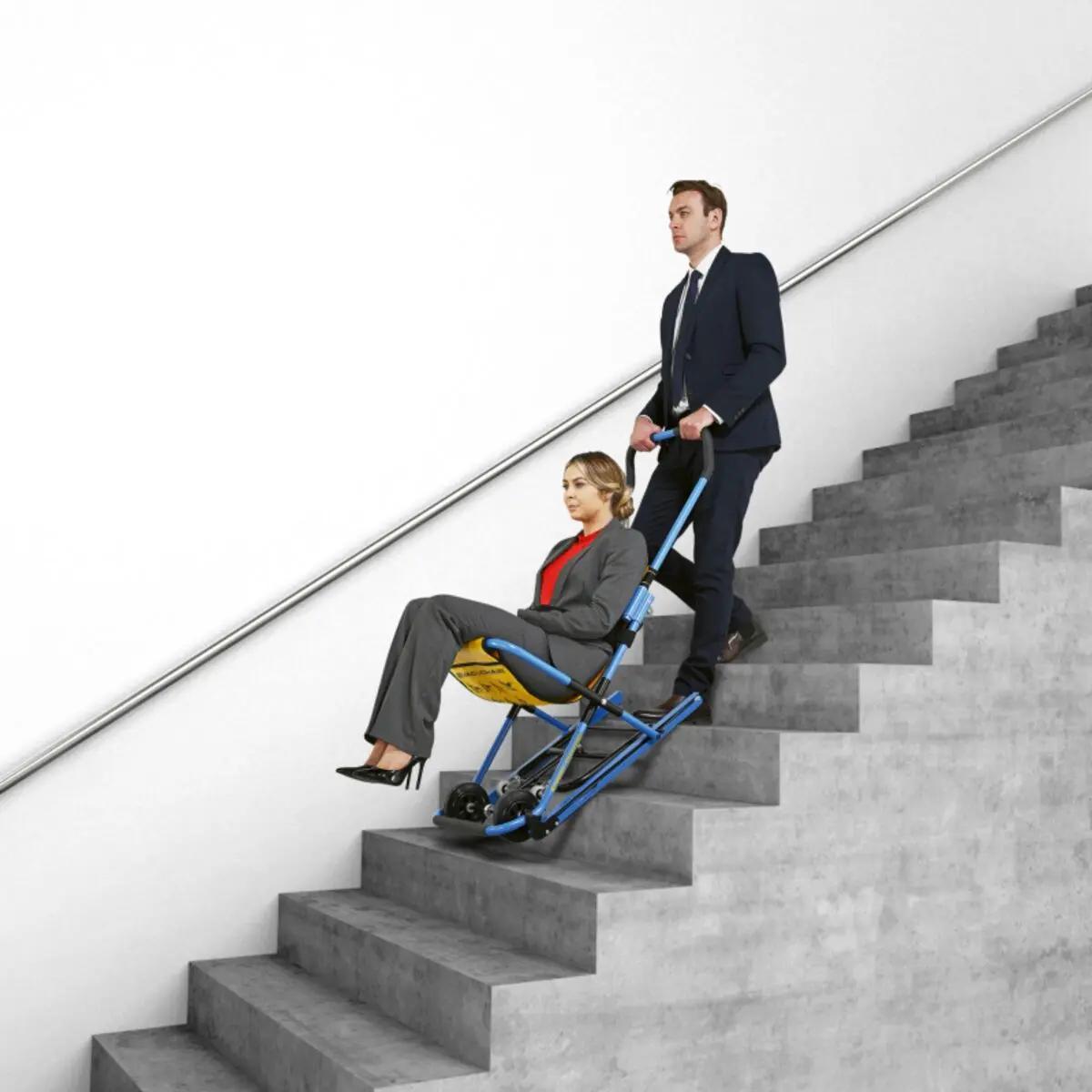 Ein Mann steigt eine Treppe hinauf, während eine Frau auf dem Evakuierungsstuhl EVAC+CHAIR 300H sitzt und von ihm begleitet wird.