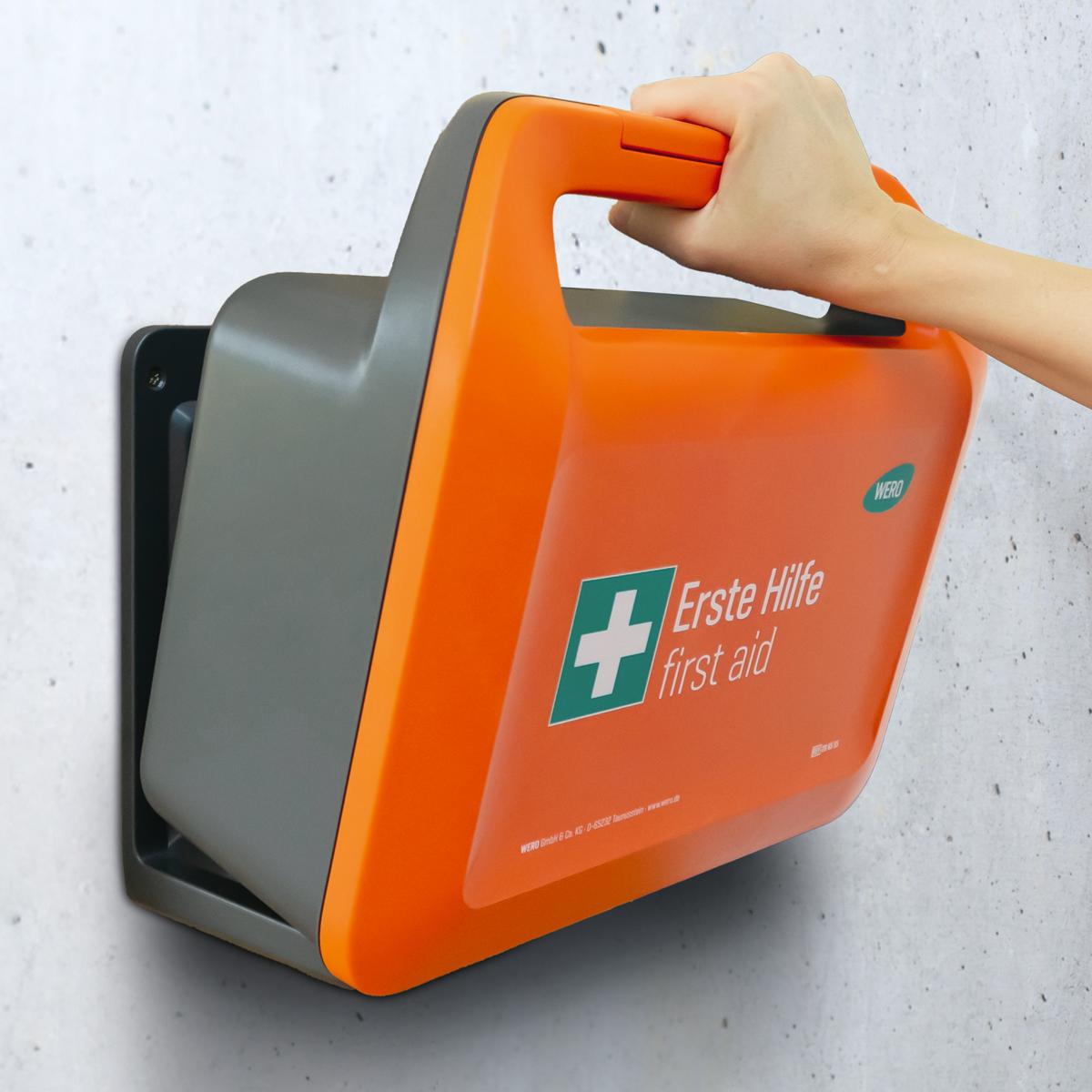 Oranger WERO Smart Case® - Erste-Hilfe-Koffer DIN 13157 - Chemie mit weißem Kreuz, grauem Sockel und grünem Logo, wird von Hand gehalten.