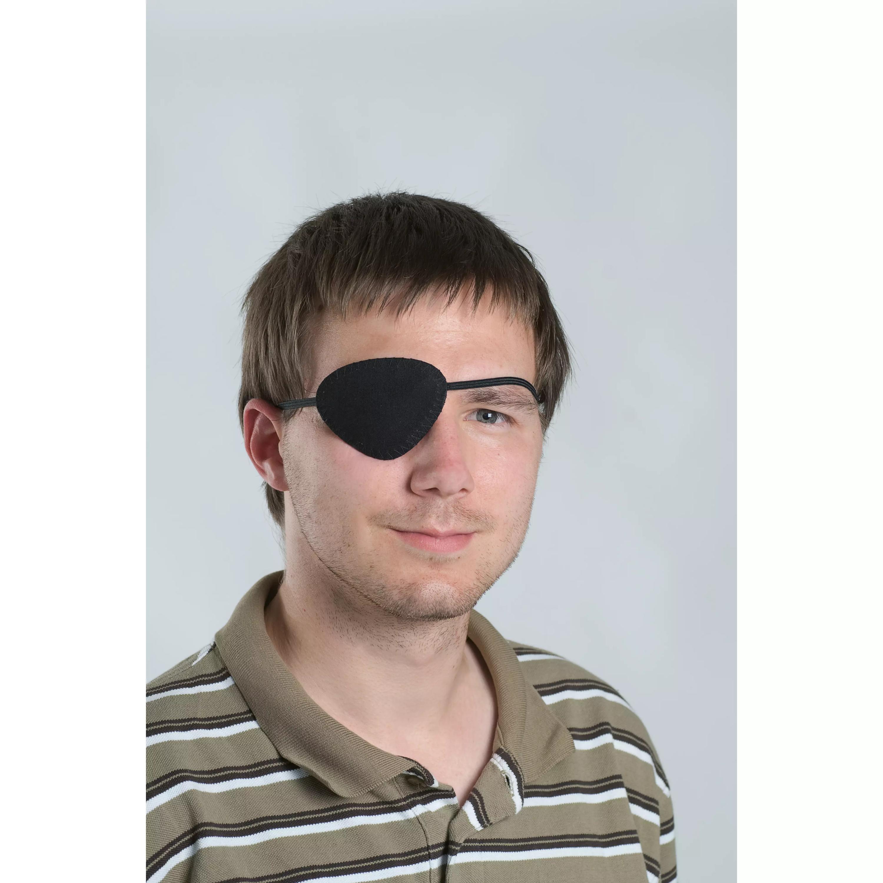 Ein junger Mann trägt eine schwarze Augenklappe mit flexiblen Befestigungsband aus Baumwolle, die sich optimal an seine Gesichtskonturen anpasst.
