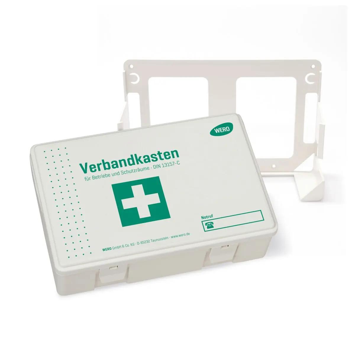 WERO Verbandkasten DIN 13157-C mit grünem Kreuz und Beschriftung, rechteckig, kompakt, steht neben passender weißer Wandhalterung.