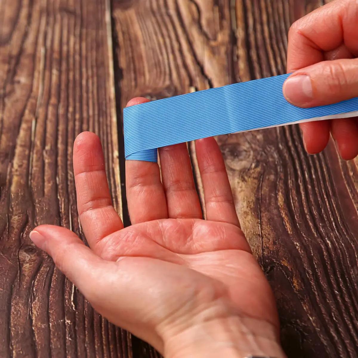 Eine Hand hält ein leuchtend blaues Werosmart® AquaFlex Detect Fingerpflaster über dem Mittelfinger; die Folie ist wasserdicht, ölbeständig und detektierbar.