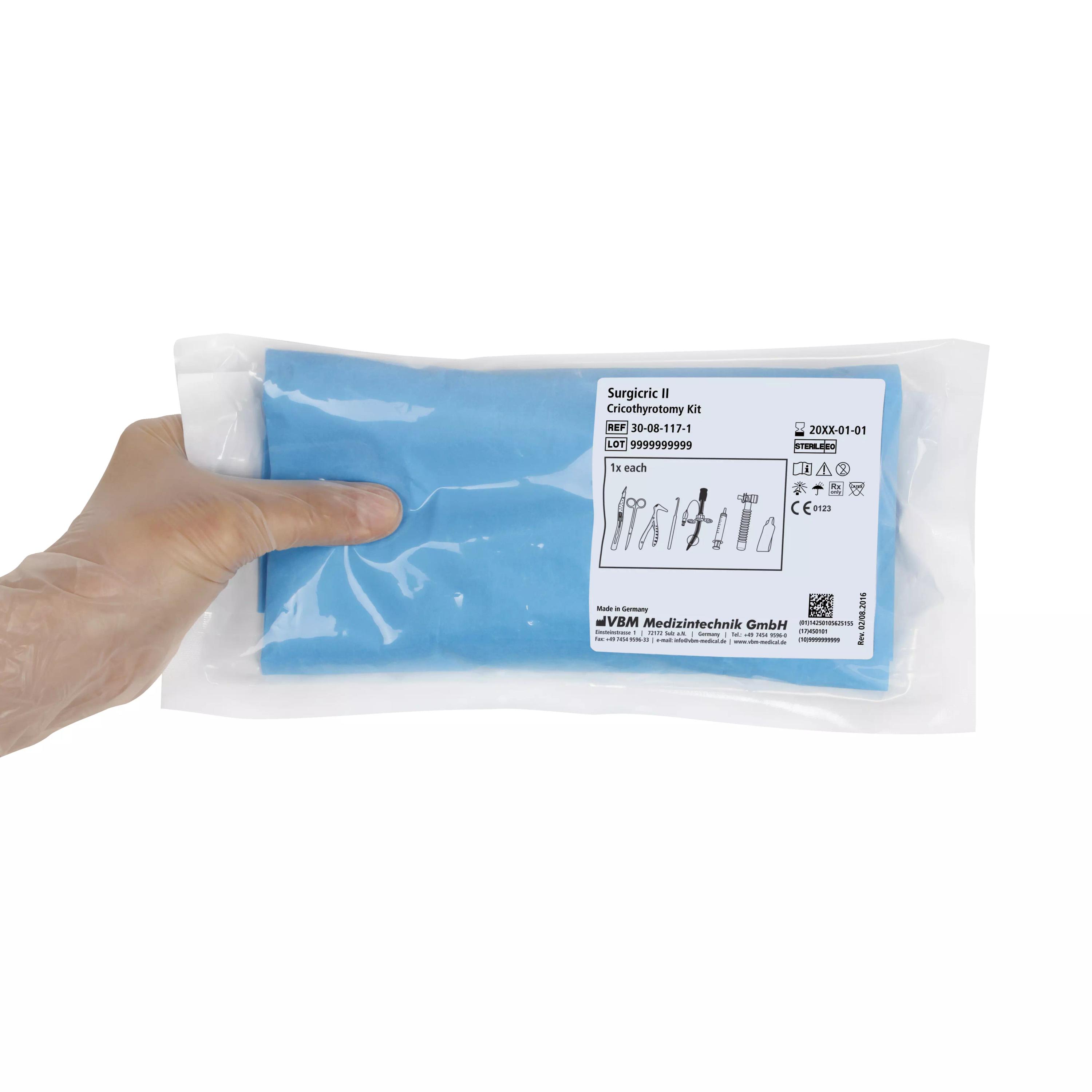 Eine behandschuhte Hand hält ein VBM Surgicric II Chirurgisches Koniotomie-Set in transparenter Verpackung mit zentralem blauen Etikett und Komponentenübersicht.