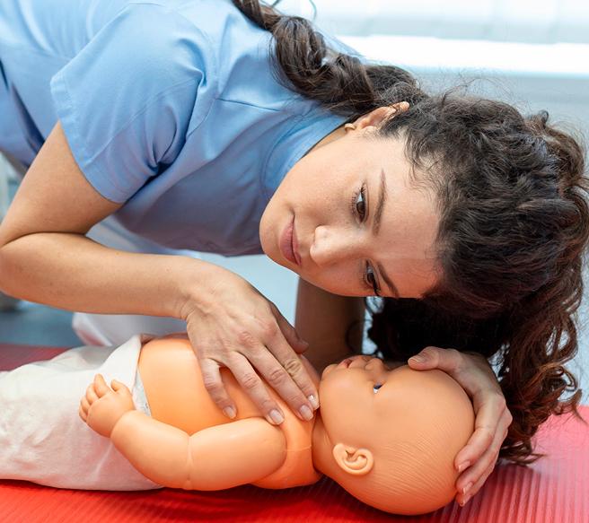 Eine Frau in hellblauer Pflegekleidung übt Erste-Hilfe-Maßnahmen an einer Baby-Puppe auf einer roten Trainingsmatte.