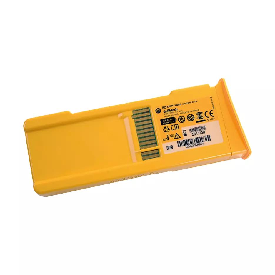 Defibtech Lifeline AED Batterie in rechteckiger, gelber Kunststoffhülle mit seitlichem Luftauslass und Etikett mit Produkt- und Prüfzeichen.