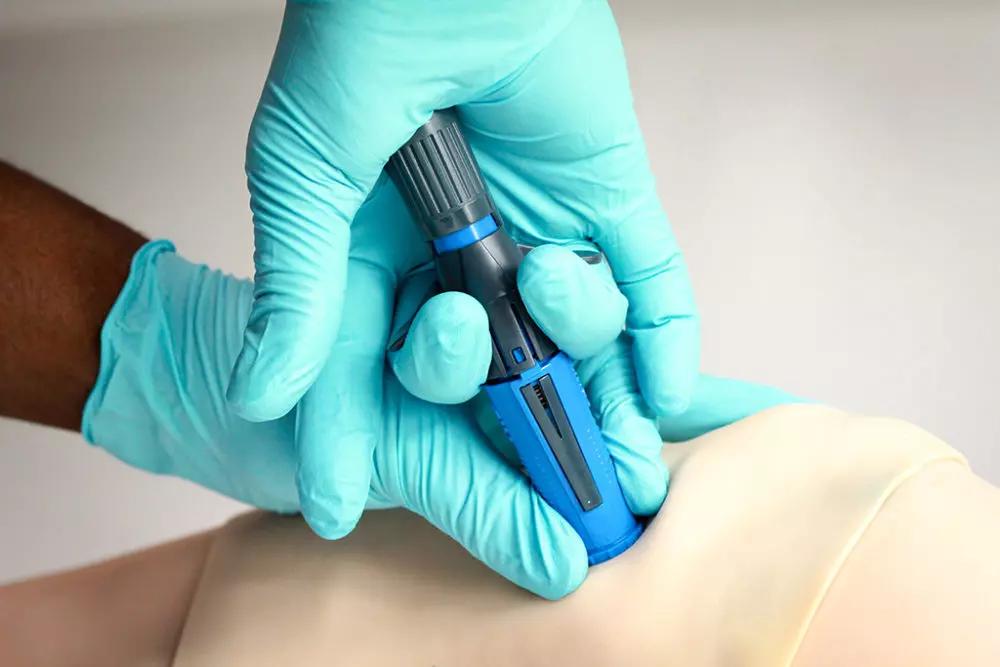 Eine Hand in blauen Handschuhen setzt den NIO-Adult - Intraossärer Zugang präzise in die Haut eines Patienten ein.